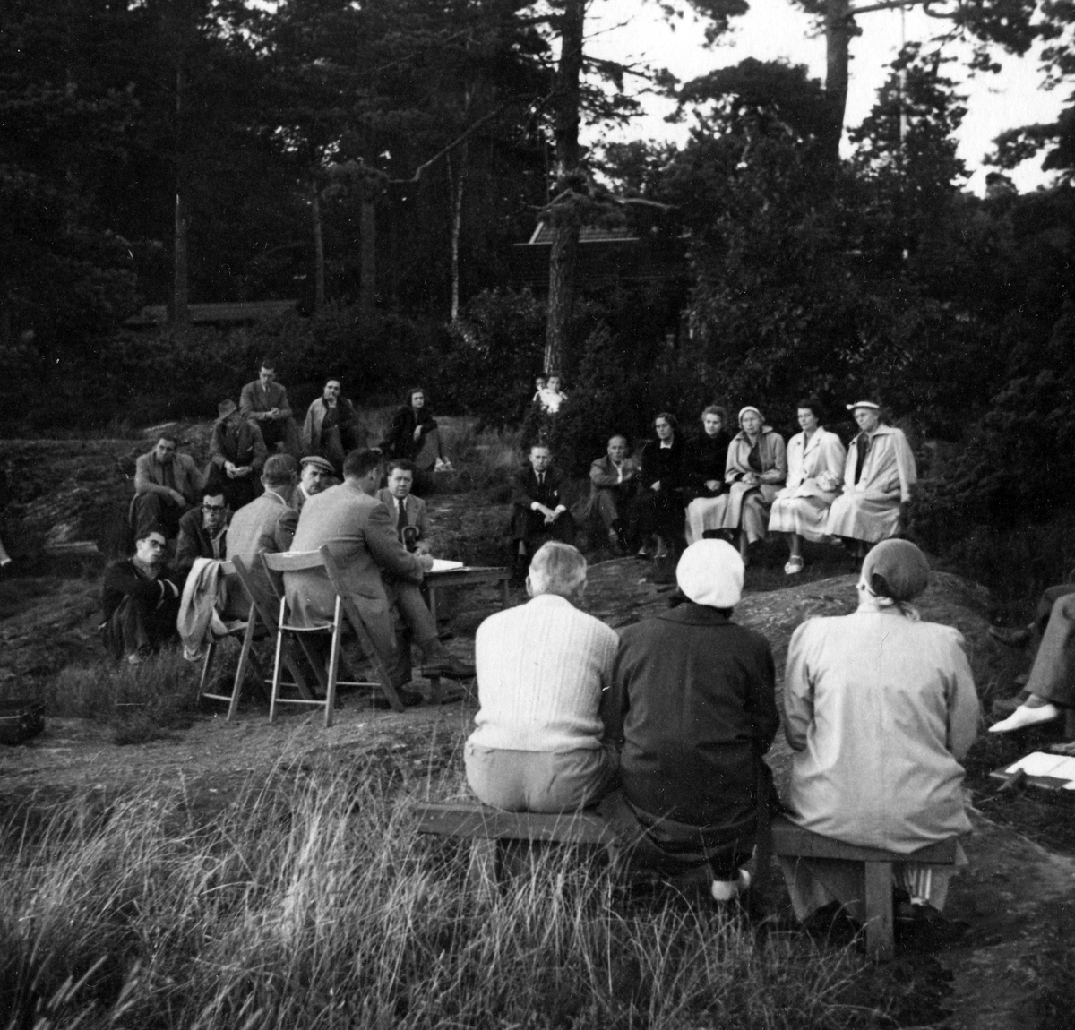 Ett tjugotal personer på ett årsmöte vid strandkanten 1954. Anteckning på kortets baksida: "Årsmöte 1954".