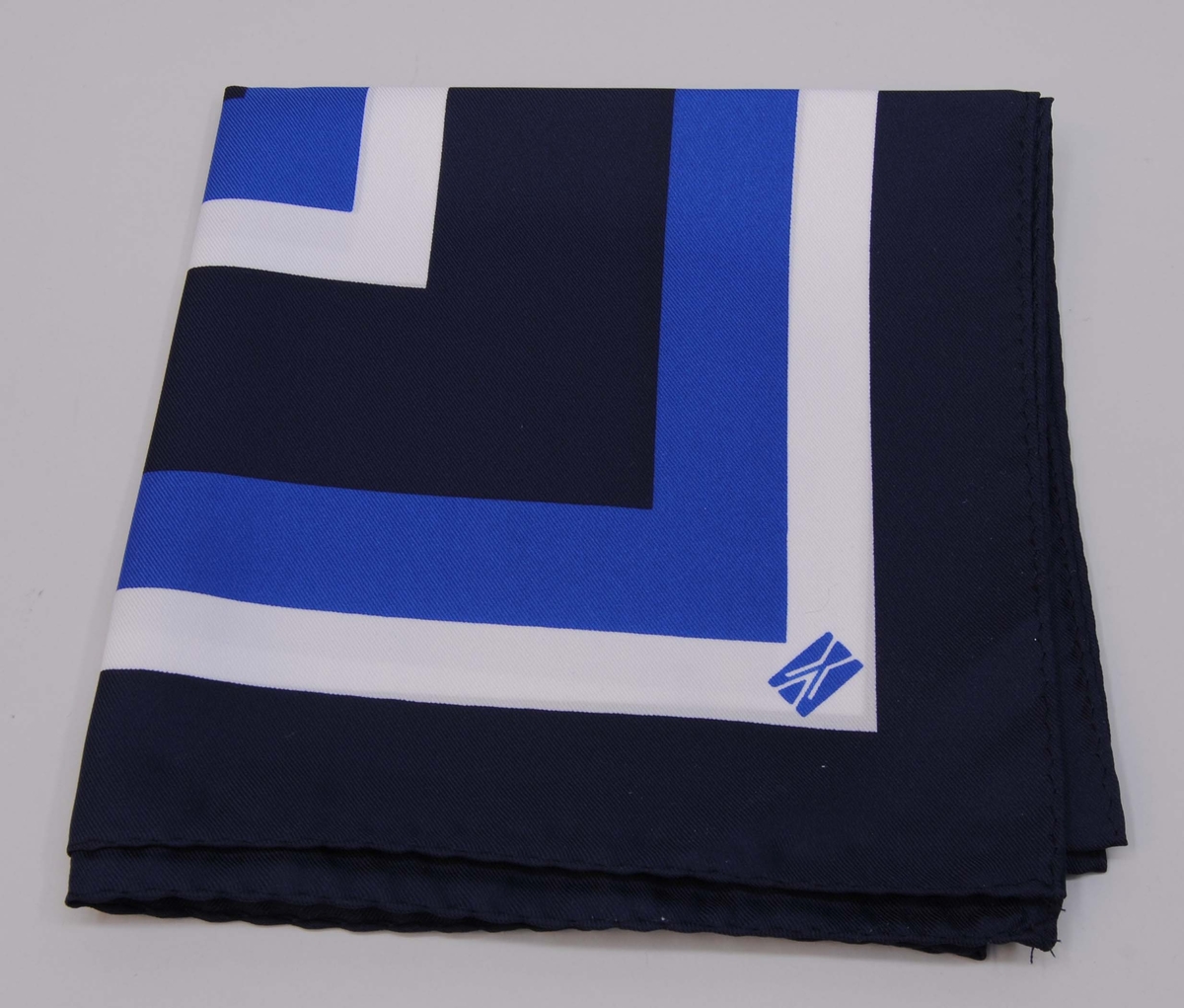 Scarf (:1) av polyester i mörkblått, blått och vitt med Banverkets logotyp. Förvaringsetui av vit kartong (:2).