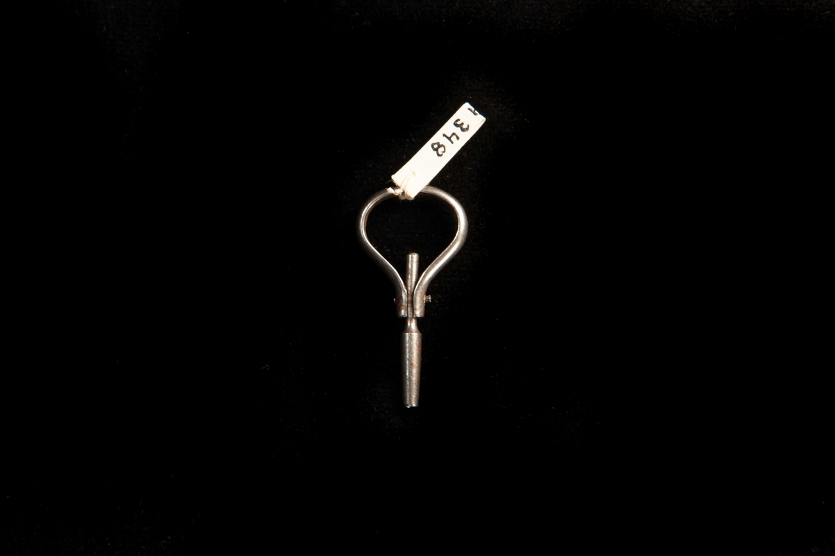 En urnyckel av metall, där handtaget är en ögla som sitter med en liten nit. Nyckeldelen går att fälla in helt in i handtagsringen.