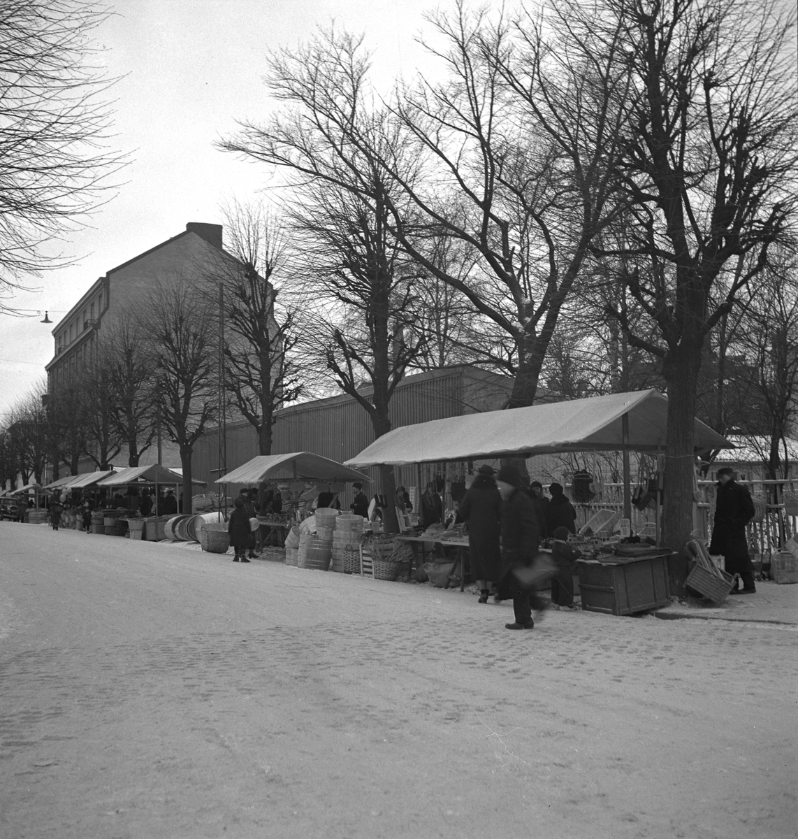 Hindersmässan i Örebro den 28 januari 1937. Försäljning pågår vid marknadsstånden utmed Stortorgets norra sida. I bakgrunden skymtar de Atterlingska basarerna.