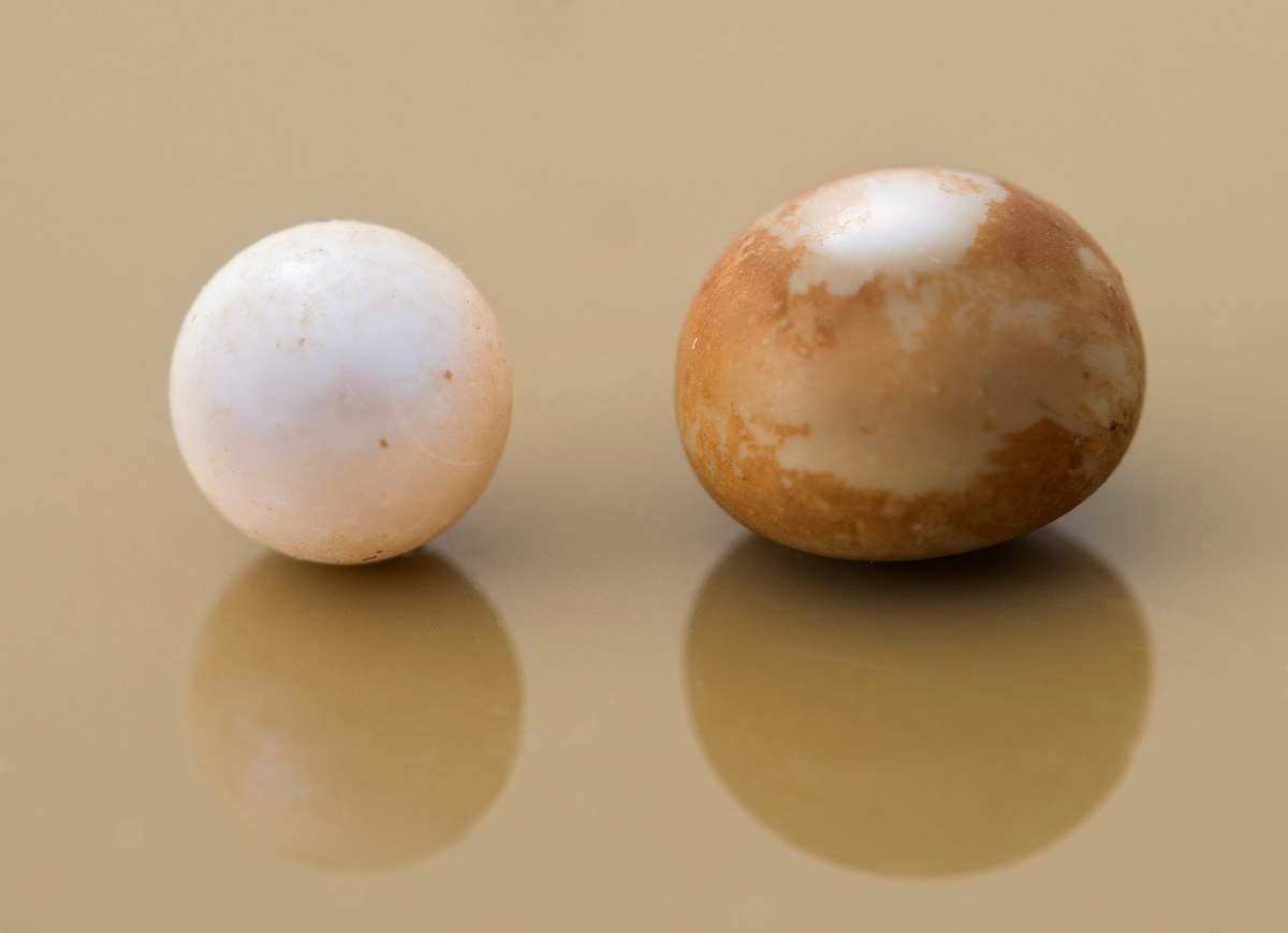 2 perler fra elvemusling: en hvit og en som er gråbrun og blank. Den gråbrune og blanke har en diameter på cirka 7 mm. Den blanke er målt til cirka 5 mm i diameter. Begge perler har en rund form. 