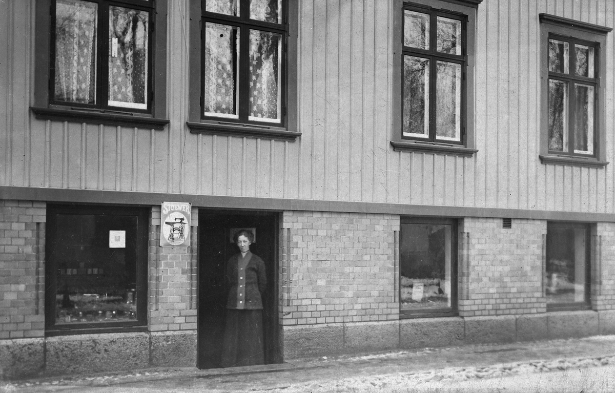 Fritz Johanssons maskinaffär på Drottninggatan 14 i Alingsås. Ebba Johansson, Fritz Johanssons fru, står  i entrédörren till affären. Senare blev här en specariaffär, bosättningsaffär och jaktvapenaffär.