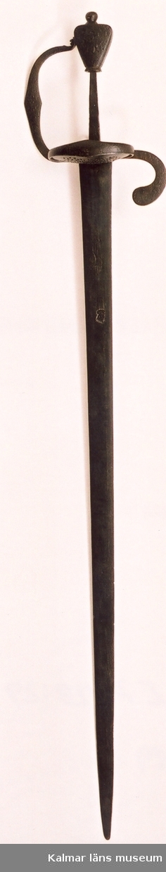 KLM 6589. Värja, av järn. Rak tveeggad klinga med linsformig genomskärning. På båda sidor återfinns Johannes Wundes (Solingen 1560-1610) stämpel (ett krönt huvud), på terssidan dessutom ulvmärke och ett riksäpple med dubbelt kors och SS. Fäste av järn med punsad ornering (serafhuvud, blad och blommor). Genombruten parerplåt, bakre parerstång, handbygel och tumring i ett stycke. Flat päronformig knapp, ornerad. Datering, från 30-åriga krigets tid.
