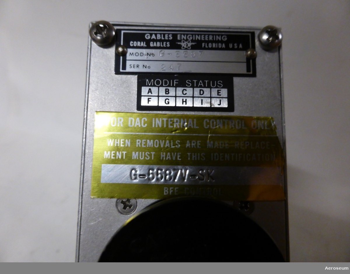 En transponder i metall. På föremålet sitter en vit post-it lapp där det är skrivet med blyerts: "MD80 NO 2". 

På baksidan sitter en streckkodslapp där det står "SAS [streckkoden] 685532 2026". Det finns även ett svart gummi/plastlock där det står: "CAPLUGS EC-20 MS90376-20R NAS813-20". 

På baksidan sitter det även en skylt där det står: "GABLES ENGINEERING CORAL GABLES FLORIDA USA", "MOD NO G5587", och  "SER NO 247". Det finns en gul klisterlapp också där det går att läsa: "FOR DAC INTERNAL CONTROL ONLY", och "WHEN REMOVALS ARE MADE REPLACEMENT MUST HAVE THIS IDENTFICATION. G-5587V-SK".