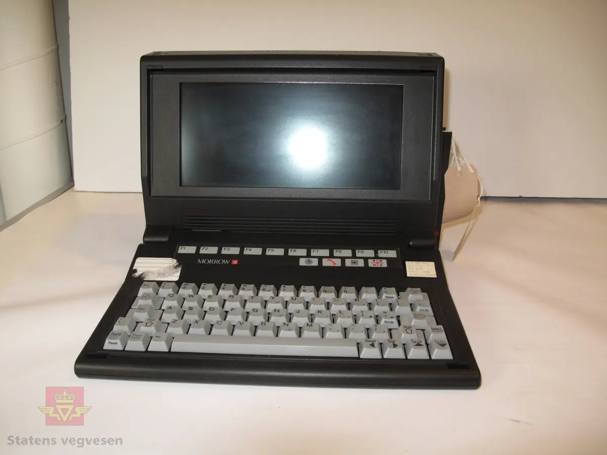 Bærbær, svart datamaskin. Det kan felles ut et tastatur, displayet er på den innvendige delen av kassen.