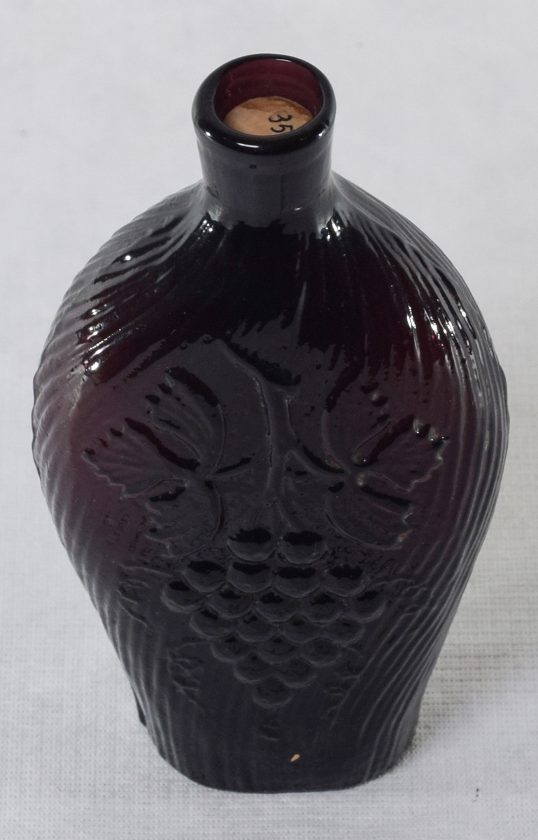 Glass, fiolett, riller, løve på ene sida og drueklase på den andre. Støperand.

Brennevinsflaske som vanligvis kalles "løveflaske". Laget på et av de norske glassverkene, annen halvdel av 1800-tallet.