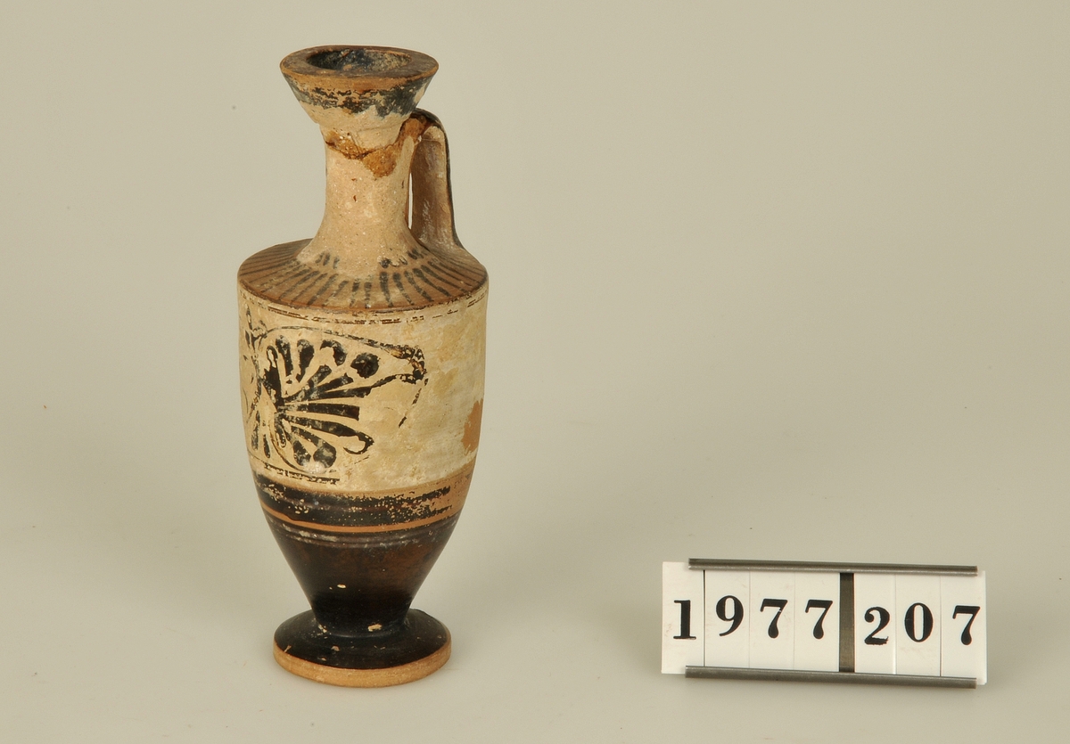 
Flaska av keramik och ett öra. Svartfigurig dekor och en påklistrad etikett med texten "Acropolis".