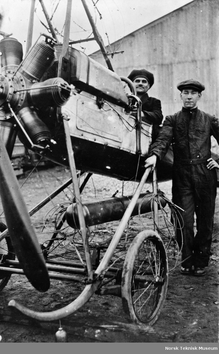 Jul. Hansen i cocpiten og mekaniker Josef Haug ved siden av Deperdussin maskinen (NTM 1345) med 50 HK Gnome roterende stjernemotor ved Sporveishallene på Majorstuen