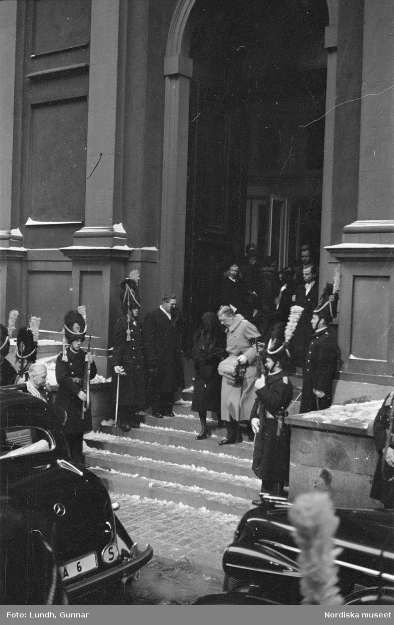 Troligen begravningen av Prins Gustaf Adolf, en kista bärs ut från Storkyrkan, kungafamiljen går ut från Storkyrkan, militärer i uniform står i givakt, kistan står på en katafalk som dras av hästar, en folksamling står längs vägen när begravningsföljet passerar.