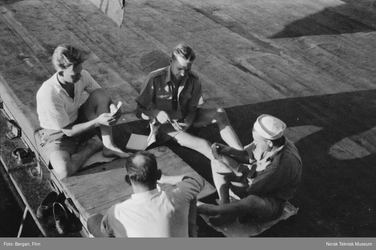 Kortspill på skipsdekk, fire personer i lav sol