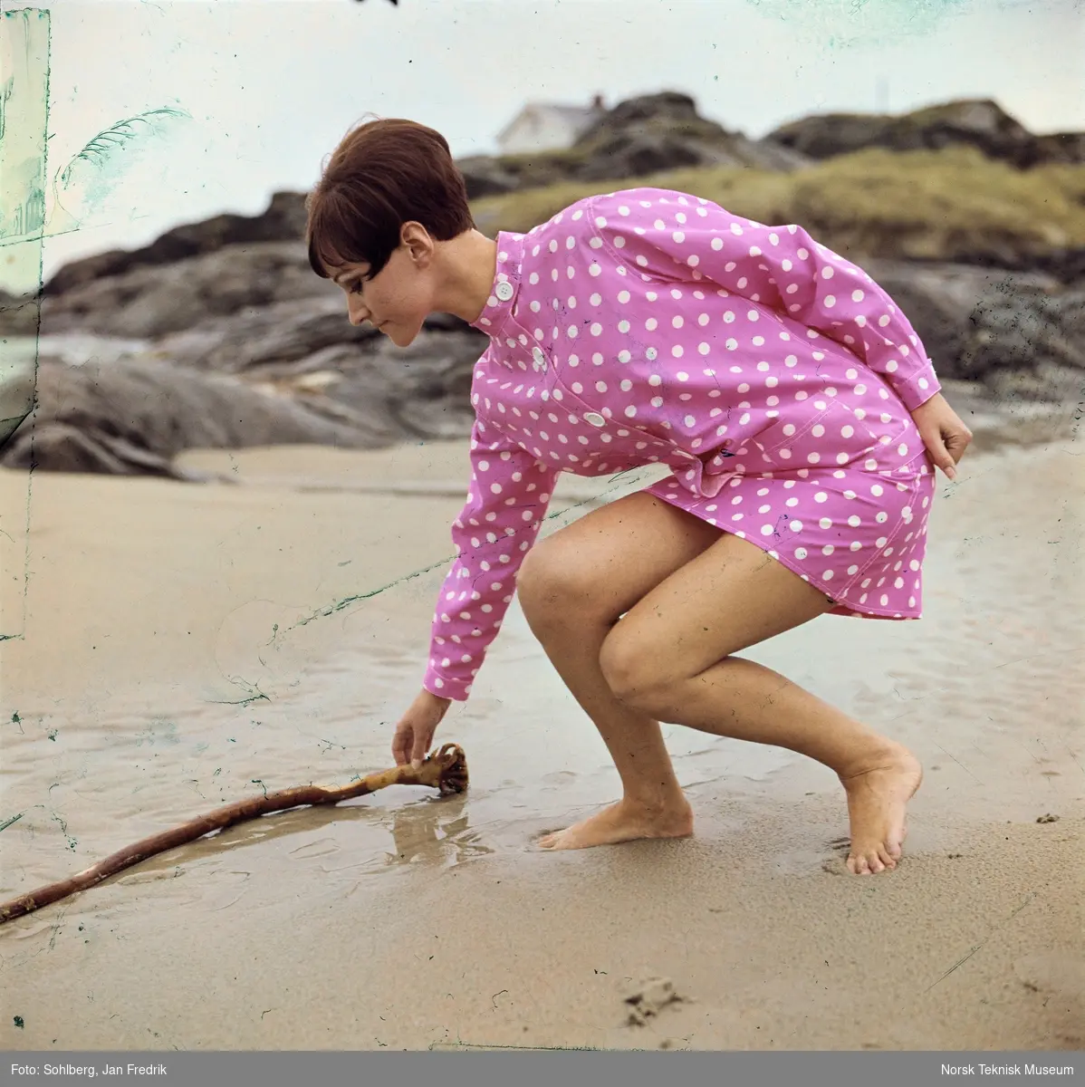 Kvinnelig modell viser bademote, hun har shorts, bikinioverdel og jakke, alt i rosa med hvite prikker. Hun er fotografert på en strand.