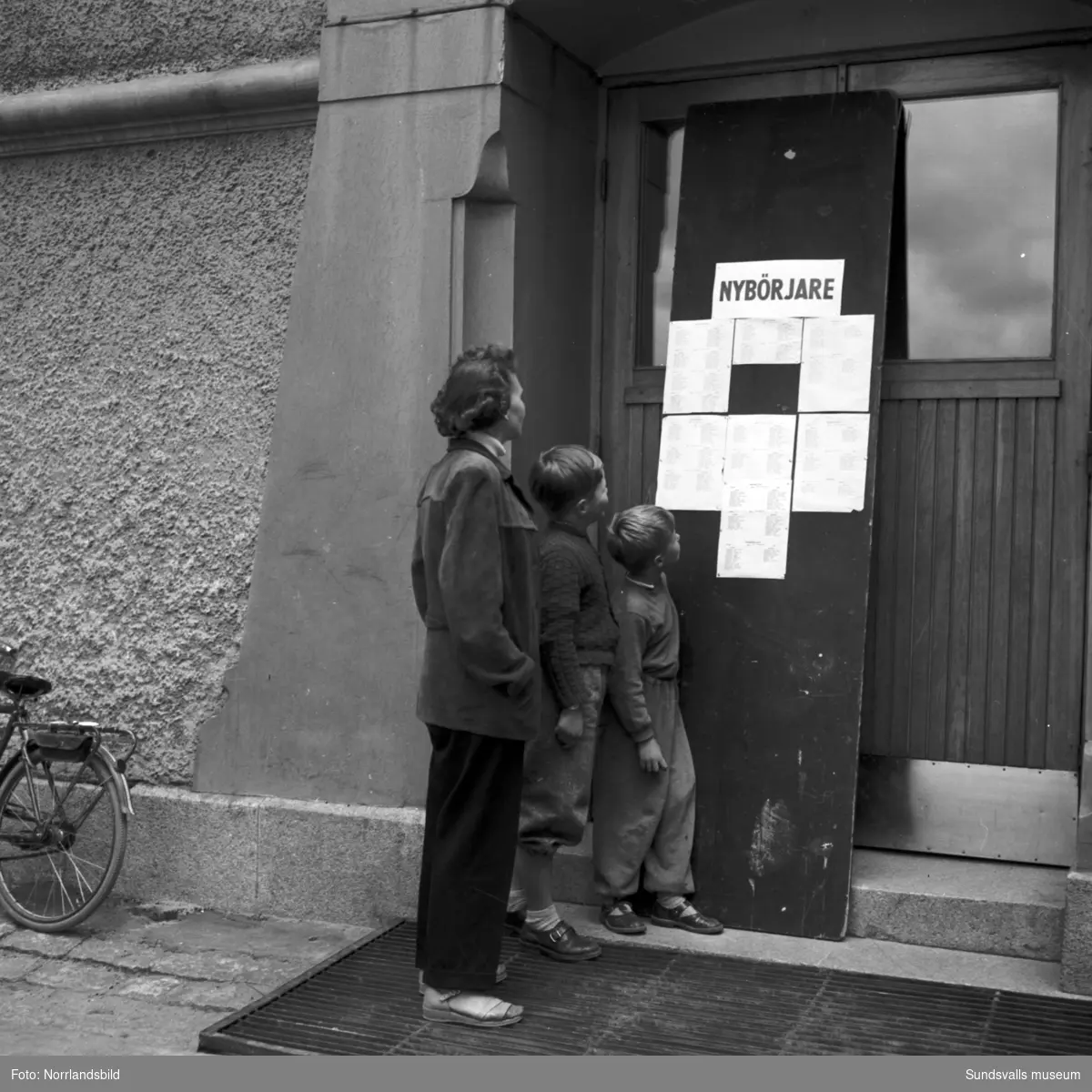 En mamma och två pojkar studerar klasslistorna för nybörjare vid GA-skolan inför terminsstarten 1952.