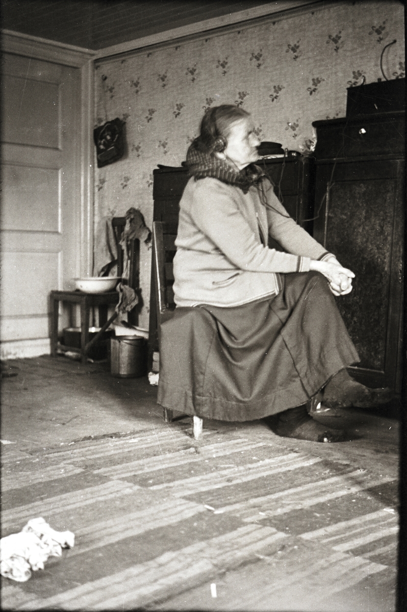 "Fållse-Maria" sitter och lyssnar på radio med hörlurar i sin stuga.