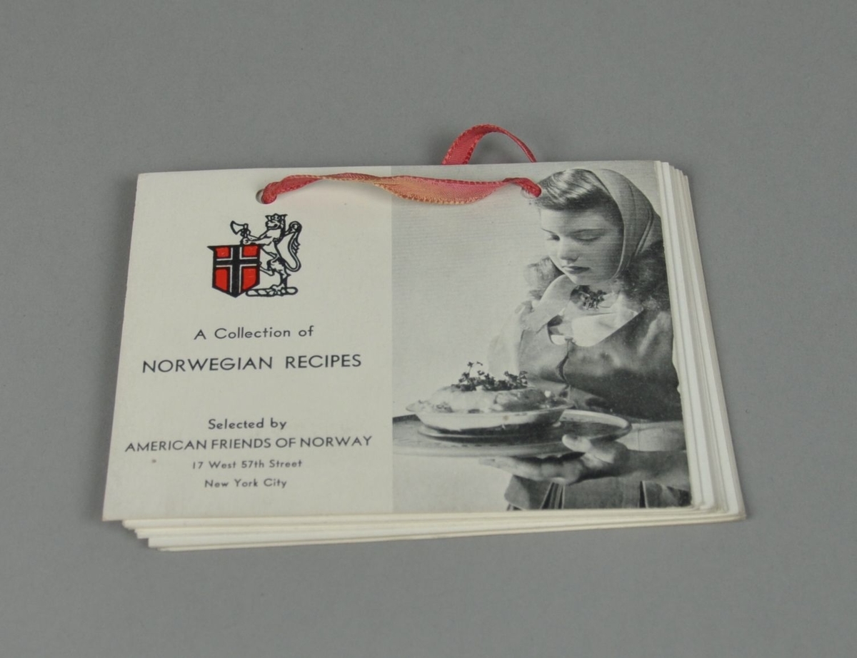 Hefte med oppskrifter. Hullede ark er bundet med bundet med rødt bånd. På framsiden er bilde av dame i norsk bunad.