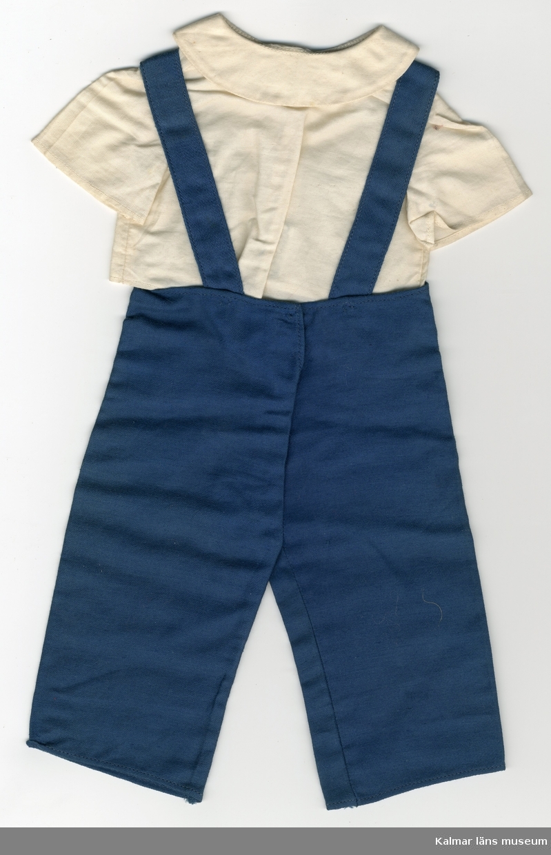 KLM 28082:127:1-2. Dockdräkt, består av hängslebyxa och skjorta. :1 Hängselbyxa, av textil, bomull, blå, två fickor nertill och bård upptill med fågelmotiv. Hängslen knäpps baktill med tryckknapp :2 Skjorta, av textil, linne, vit, kortärmad. Kragens snibbar rundade med vit knapp i mitten. Skjortan knäpps framtill med tryckknapp vid kragen.