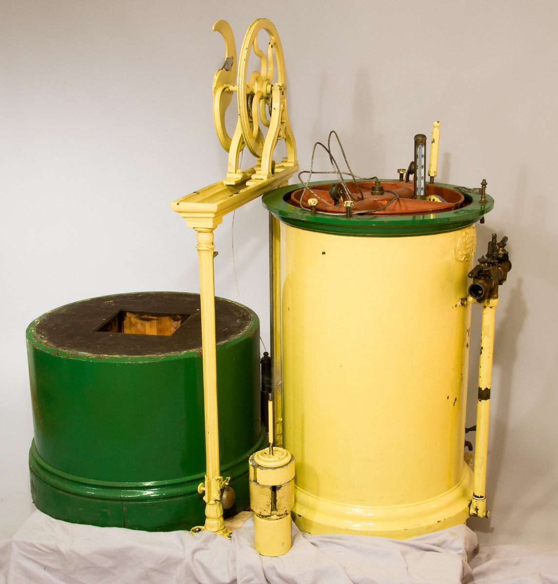 Gasklocka målad i gul och grön färg. Har texten "The gas meter Co, limited makers Oldhall works" på sig.