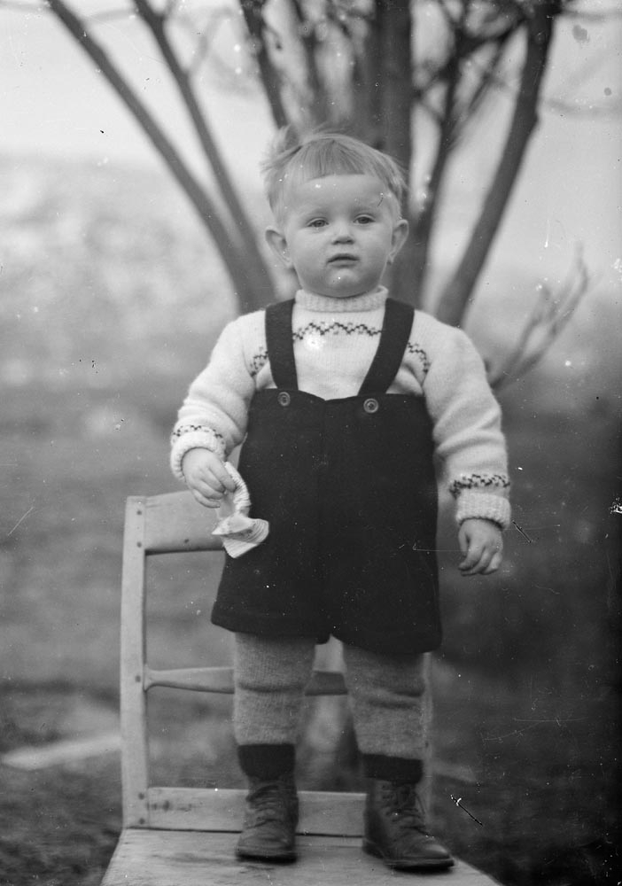 Leirfjord, Ulvangen, Myrvang. Barneportrett av Sigurd Myrvang (f. 1945). Han står på en stol og har på seg ullgenser, selebukse, ullstrømper og små skinnstøvler.