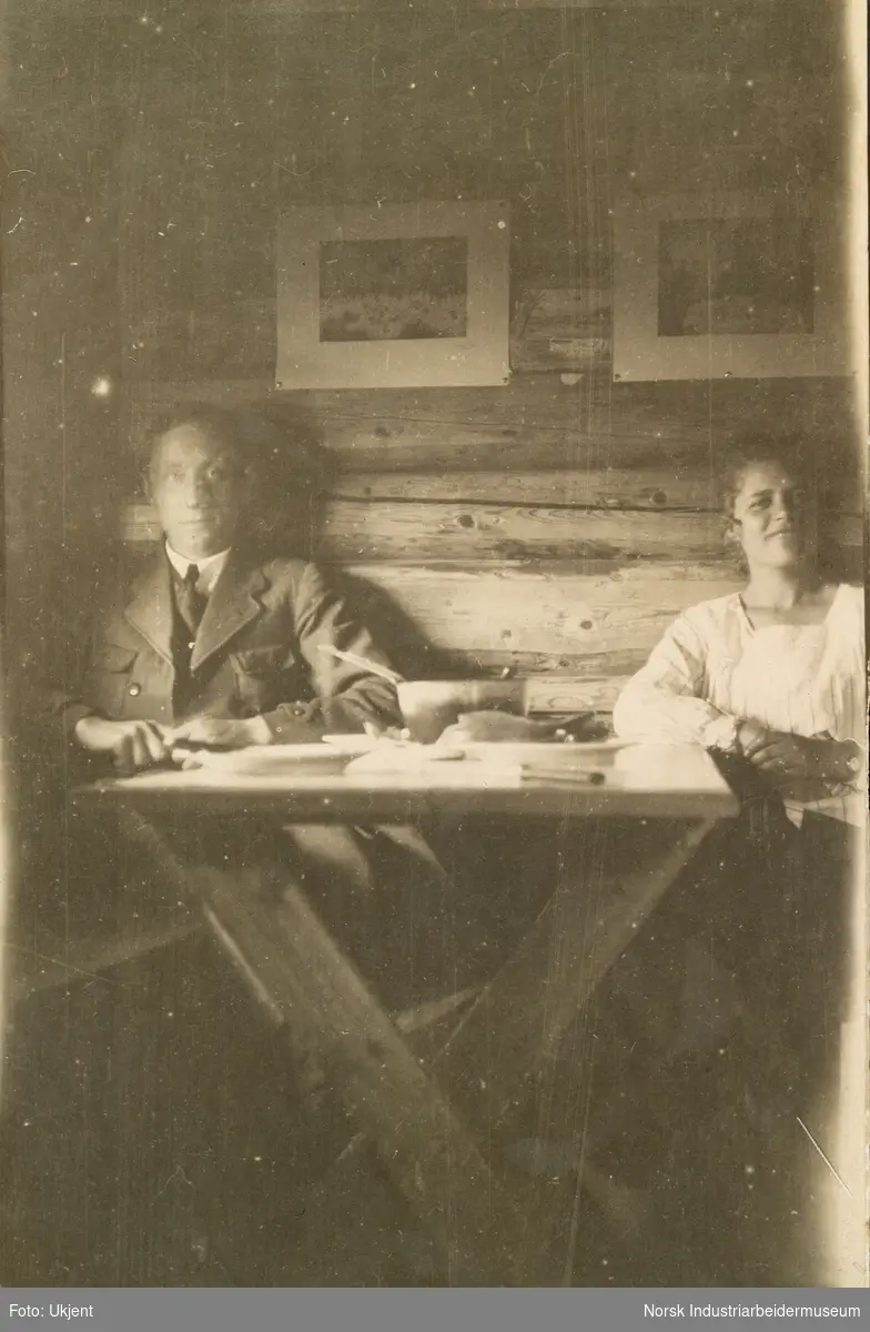 Mann og kvinne sitter mot vegg ved middagsbord