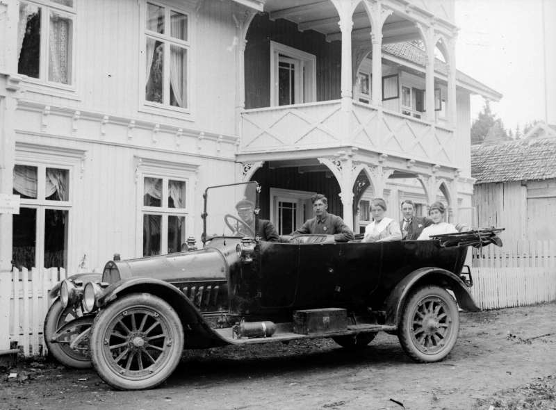 Bil av merke Opel med nedslått kalesje og fem personer foran Grand Hotel på Jørstadmoen