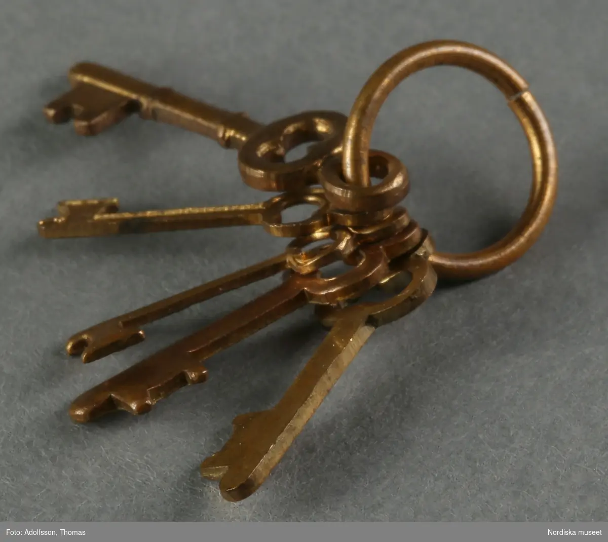 Nyckelknippa med fem metallnycklar i miniatyrstorlek.  Nyckelknippan ligger vid spegeln i hallen på första våningen i dockskåpet NM.0331721+.