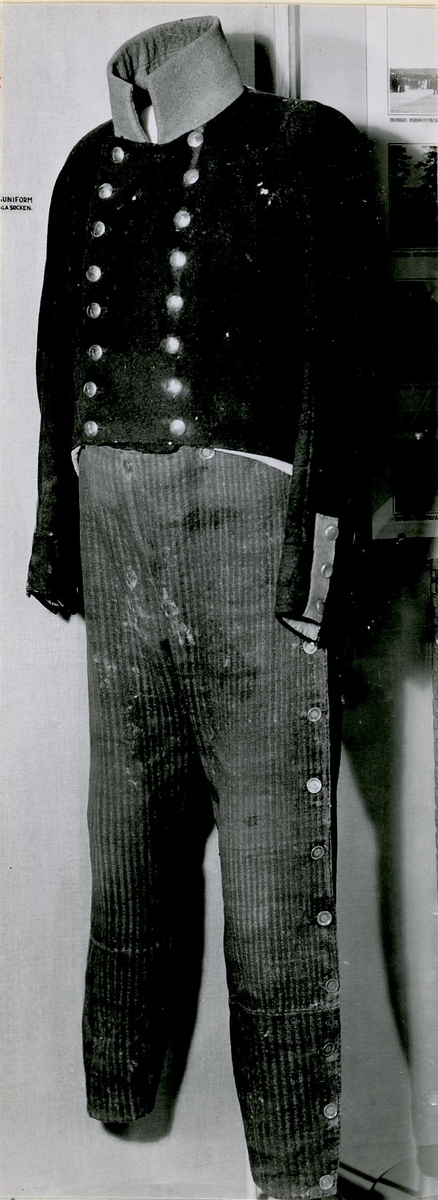 Uniformsbyxa från 1800-talet början.
Byxorna är grårandiga med knäppning i sidan med platta bronsknappar, med särskild linning av samma tyg upptill på framsidan.