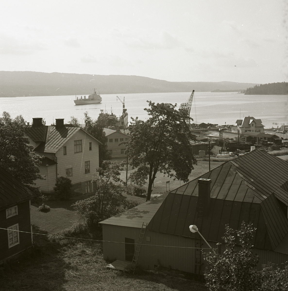 Utsikt över bostadshus och hamnen i Lunde på Sandö. I hamnen syns två kranarmar och ett fartyg är på väg in.
