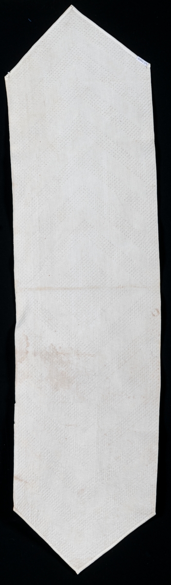 Vit badrumsmatta förmodligen vävd i sk noppväv. Kortsidorna kantade med vita band som är fastsydda med symaskin.