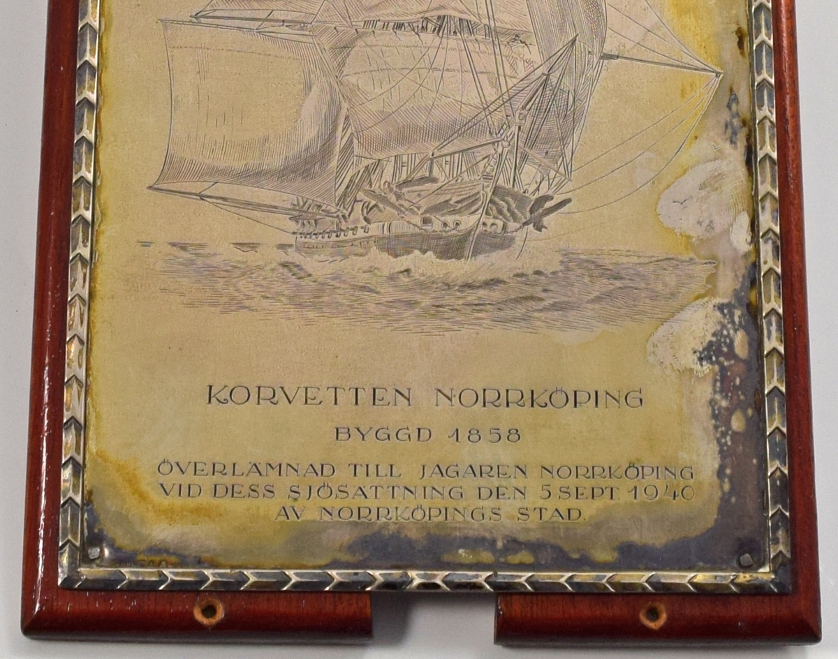 Minnesplakett av silver från jagaren Norrköpings sjösättning (silverstämpeln svår att tyda). Monterad på platta av mahogny. I metallen finns korvetten Norrköping ingraverad.