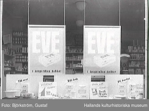 Skyltfönster till Kooperativa AB, butik i Varberg. Hela skyltfönstret tillägnas margarin av märket Eve. "Eve - i kooperativa butiker. Till mat, till bak, på bordet" förkunnar skyltarna. Eve började tillverkas av kooperationen 1921 och namnet är en förkortning för "Extra Vitaminberikat".