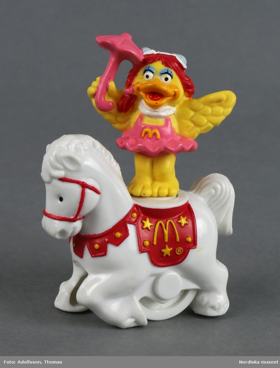 Mekanisk leksak som föreställer en flickkyckling klädd i rosa balettkjol och med ett parasoll i handen. Figuren balanserar på en vit häst med ett hjul på undersidan. När man drar hästen mot underlaget snurrar flickan. McDonald's logotyp, ett stort M, finns på både hästen och flickan.