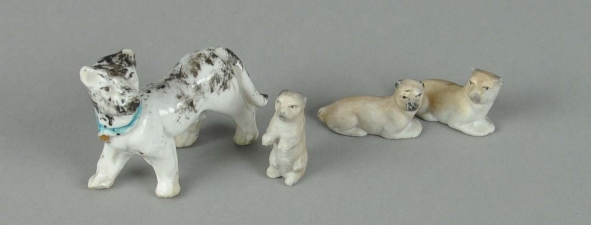 Fire hundefigurer av porselen. En hund står på alle fire og har glassert keramikk. To hunder ligger, og en hund står på bakbeina.