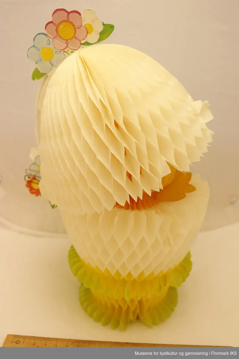 En utfoldbar papirfigur av en påskekylling i skallet sitt. Skallet kan foldes over hodet på kyllingen, og festes på plass ved bruk av binders. Hele figuren kan foldes flat