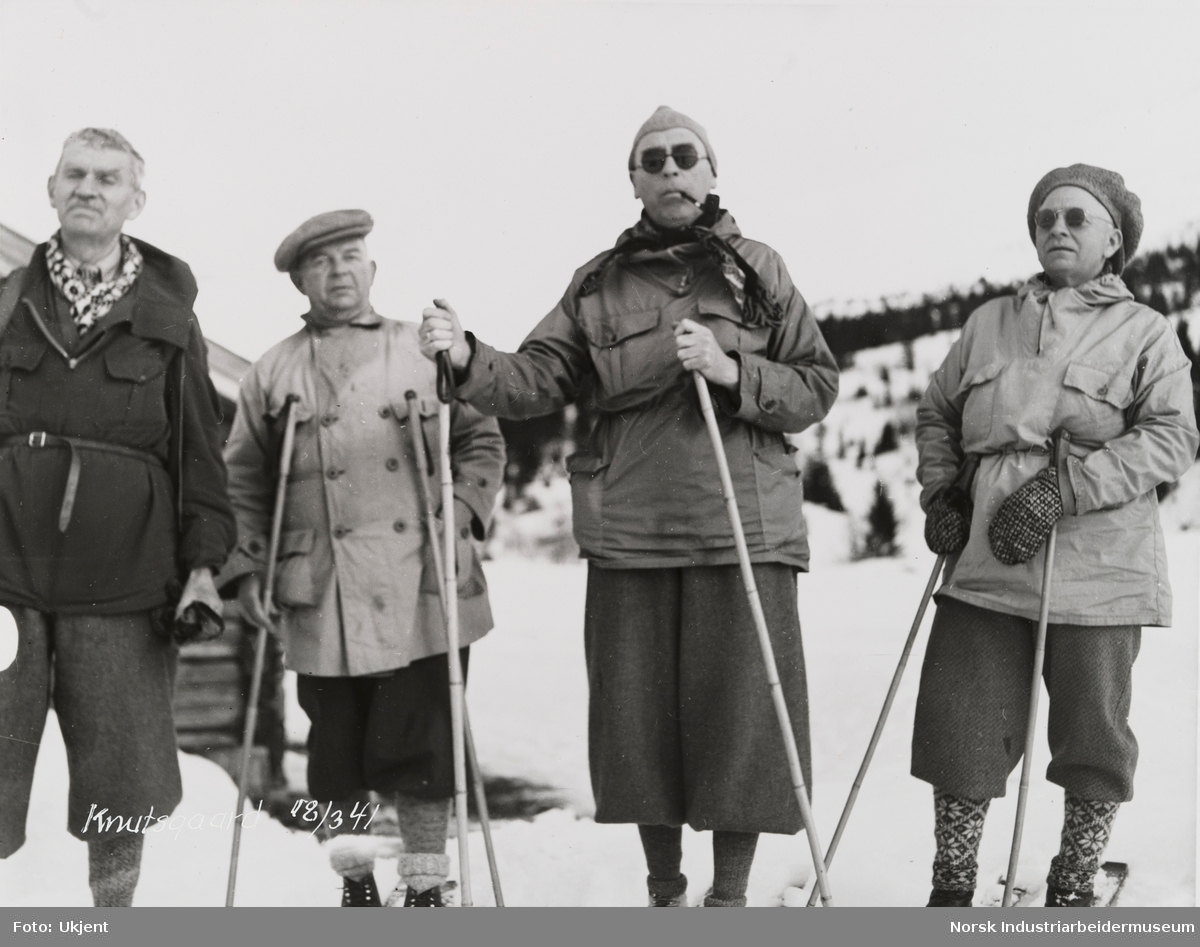 Fire menn utstyrt med turklær, lue og solbriller på skitur i fjellet