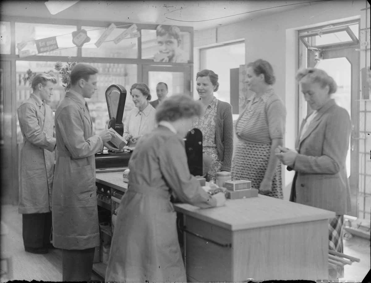 Butikspersonal hjälper kunder vid kassadisken, Konsum, Harg, Uppland 1953