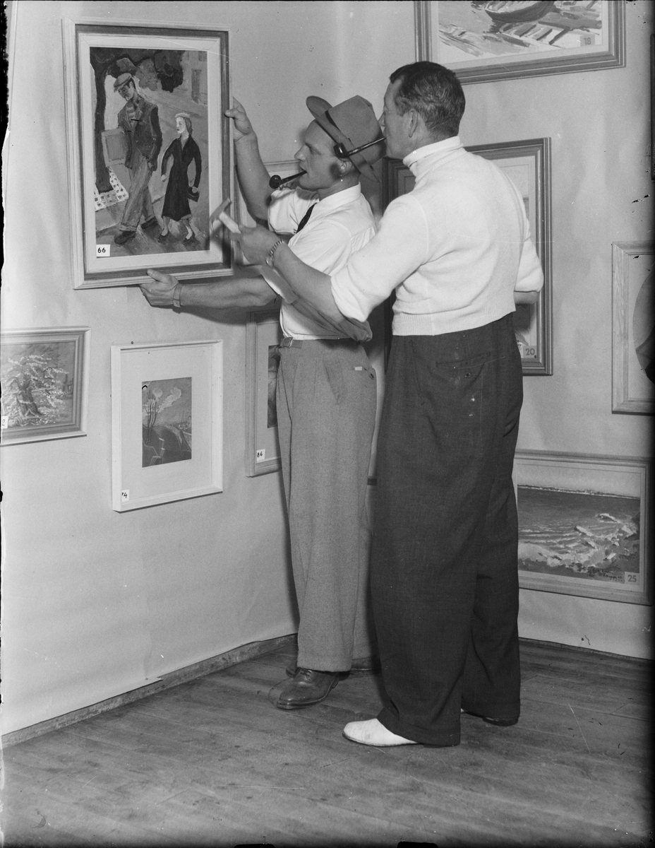 Två män placerar tavla i galleri, Östhammar, Uppland