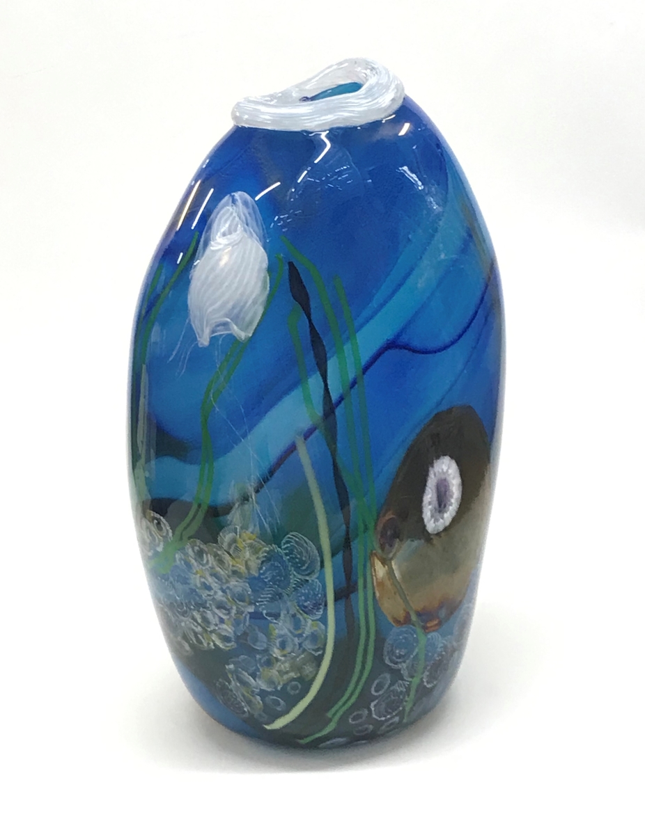 Organiskt formad vas i blått glas med havsmotiv i form av skulpterade och invälsade maneter, sjögräs och snäckor. Överst en vit mynningsrand. Två av maneterna och vissa av snäckorna  är formade av glas som reagerar på uv-ljus.