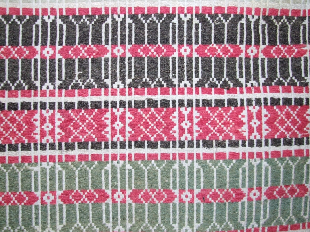 Smetta grøn frikant på raud (korsforma?) innramming midt på teppet. 