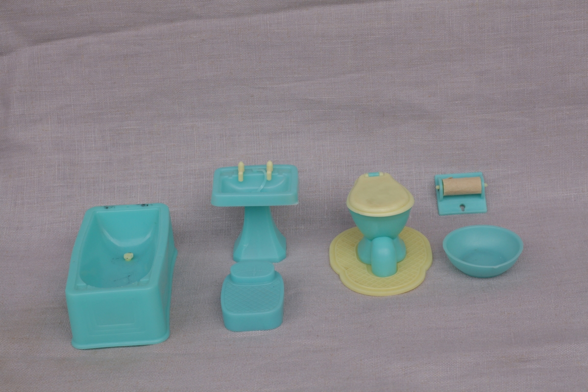 Blått og gult baderomsinventar i plast. Badekar, vask, badevekt, toalett med underlag, dorullholder og vaskefat.