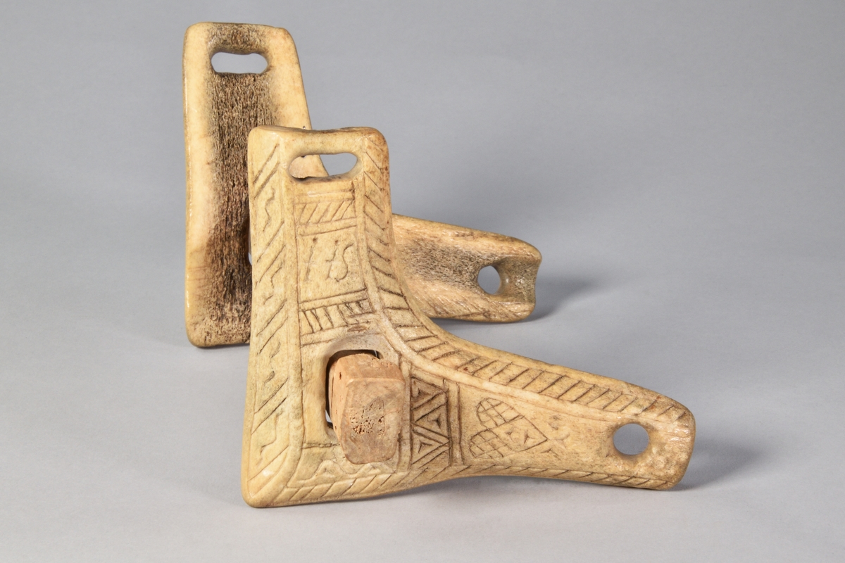 Munbett av trä, rakt, med två vinklade rörliga sidostycke av horn. Rik ornamentik på sidostyckena.