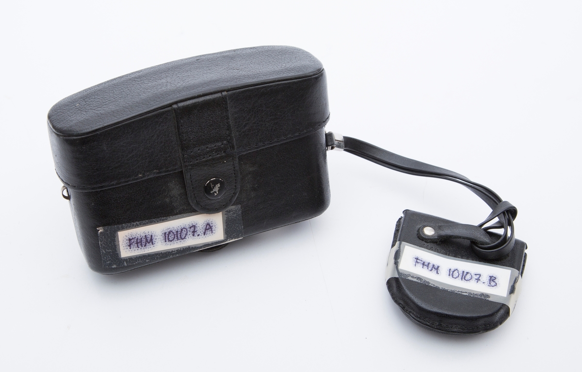 Kamera i sort skinnetui og beskyttelseslinse i skinnetui med rem satt fast på kamera. Rektangulært kamera. Mrk:"Minox 35 GL". 