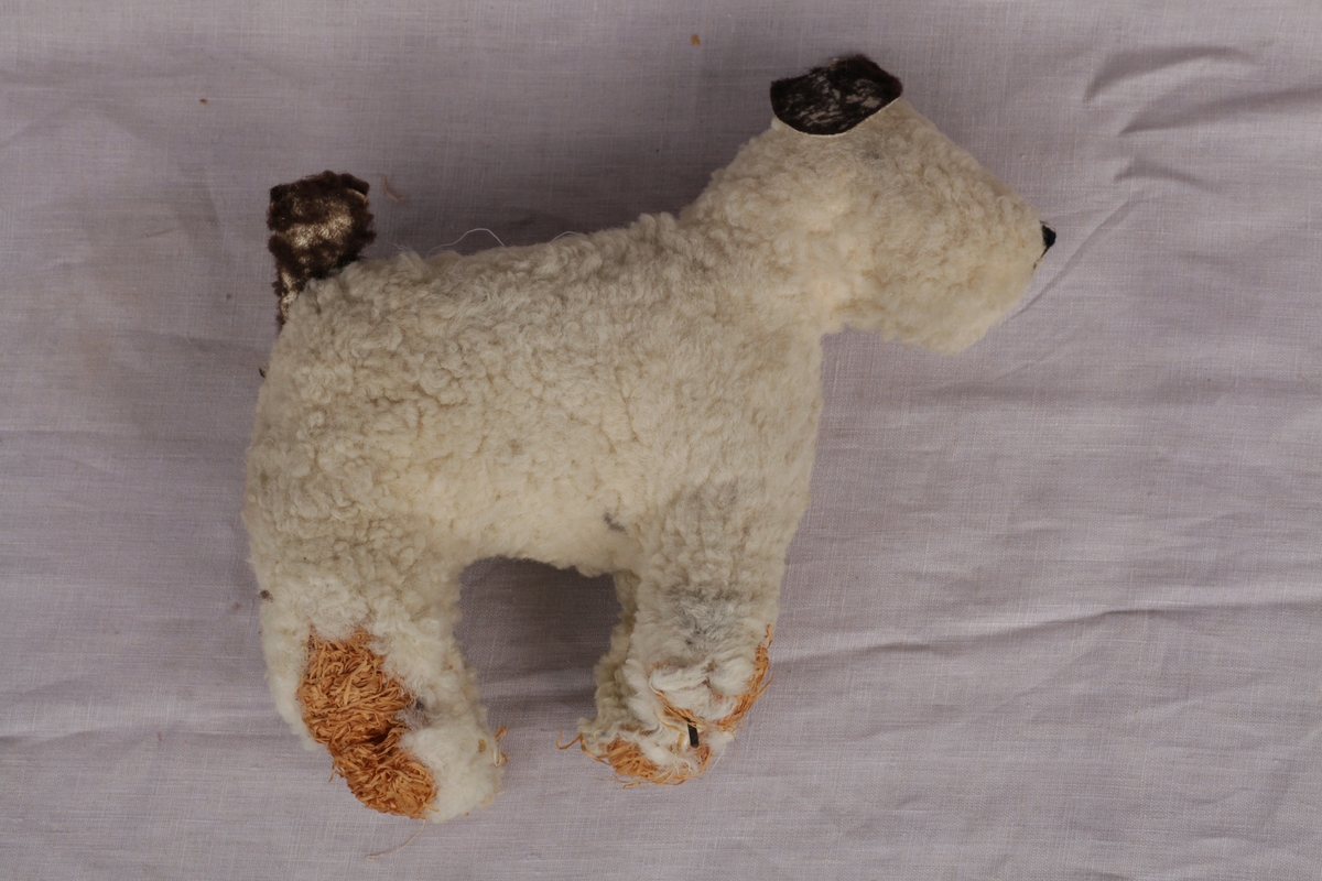 Hvit lekehund (terrier) med brune ører og brun hale. Metallramme og fylt med strå. En del slitasje på labbene, ørene og halen.