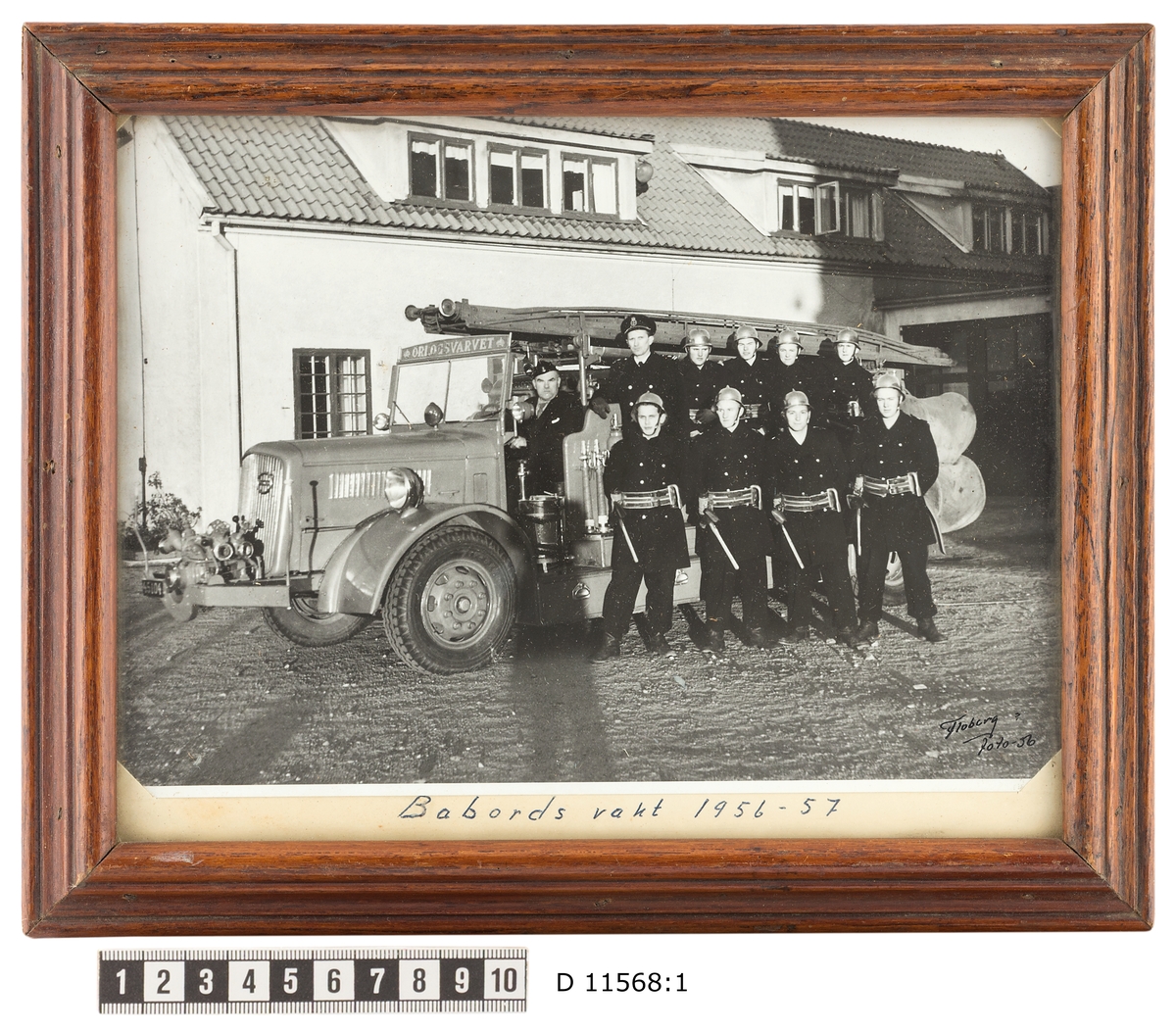 Bilden visar brandmän från brandkåren i Karlskronas örlogsvarv som har tagit uppställning för en gruppfoto framför sin brandbil och brandstationen.