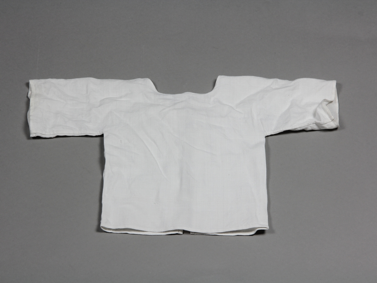 Skjorta av tunt vitt linne, för spädbarn. Knyts i ryggen med två par band.