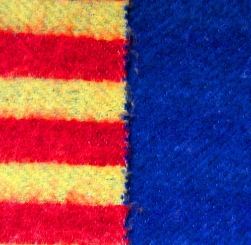 Vävprov till beklädnadstyg vävt i inslagsförstärkt kypert i ullgarn, stickgarn 8/2. Varpen är vit och inslaget är blått, rött och gult. På ena sidan är vävprovet enfärgat blått och på den andra sidan randigt i rött och gult. Ränderna är knappt 30mm breda. Vävprovet har beretts genom valkning och lätt ruggning. Vävprovet har en 45mm bred maskinfåll i vardera kortsidan.

Vävprovet är kemtvättat en gång efter en brand 2000. 

Vävprovet med modellnamn Starke är formgivet av Ann-Mari Nilsson och tillverkat av Länshemslöjden Skaraborg. Det finns ett vävprov monterat i aluminiumram, se inv.nr. 0041:14, som finns med på sidan 82-83 i vävboken Väv tyger till kläder av Ann-Mari Nilsson i samarbete med Länshemslöjden Skaraborg från 1989, ICA Bokförlag. Tyget är enligt boken lämpligt att använda till jacka eller kappa. Se även inv.nr 0041-0096 ur samma bok.