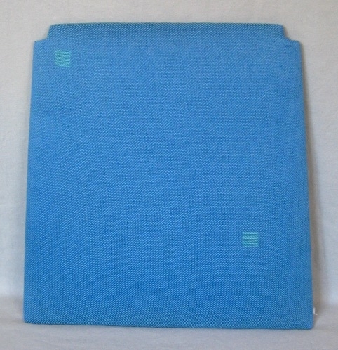 Möbelöverdrag, möbeltyg monterat på stolsdyna. Ett kraftigt och stelt möbeltyg vävt i kypert med inslagseffekt. Tyget är mönstrat med 20x20 mm stora kvadrater i varpeffekt glest utspridda. Varpen är av tunt tvåtrådigt bomullsgarn i starkt blågrönt. Inslaget är blått entrådigt lingarn tre trådar tillsammans.

Möbeltyget är monterat med häftklammer på en stolsdyna av skivmaterial, plywood, med stoppning. Dynan är lite smalare i bakkant och där är hörnen urtagna. 

Möbeltyget med modellnamn Kvadrat är formgivet av Ann-Mari Nilsson och tillverkat av Länshemslöjden Skaraborg.Se även inv.nr. 0122 och 0124 Vävprov samt 0123 kudde.

En pappersetikett är fastklistrad på baksidan av stolsdynan. Texten lyder:"Möbeltyg: kvadrat, Bredd:, Kvalite: Lin - Bomull, Pris 462:-/m".