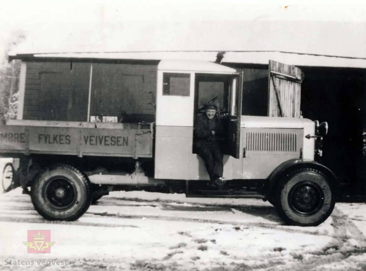 Bildet viser sjåfør Theodor Aarønes i bildøra på "Strømmen lastebil, kalt "Jernhesten". 

På bilen står "Møre Fylkes Veivesen". 

Møre var navnet på fylket fra 1919 til 1935, da det skiftet navn til Møre og Romsdal.
(Kilde: Store Norske Leksikon)

