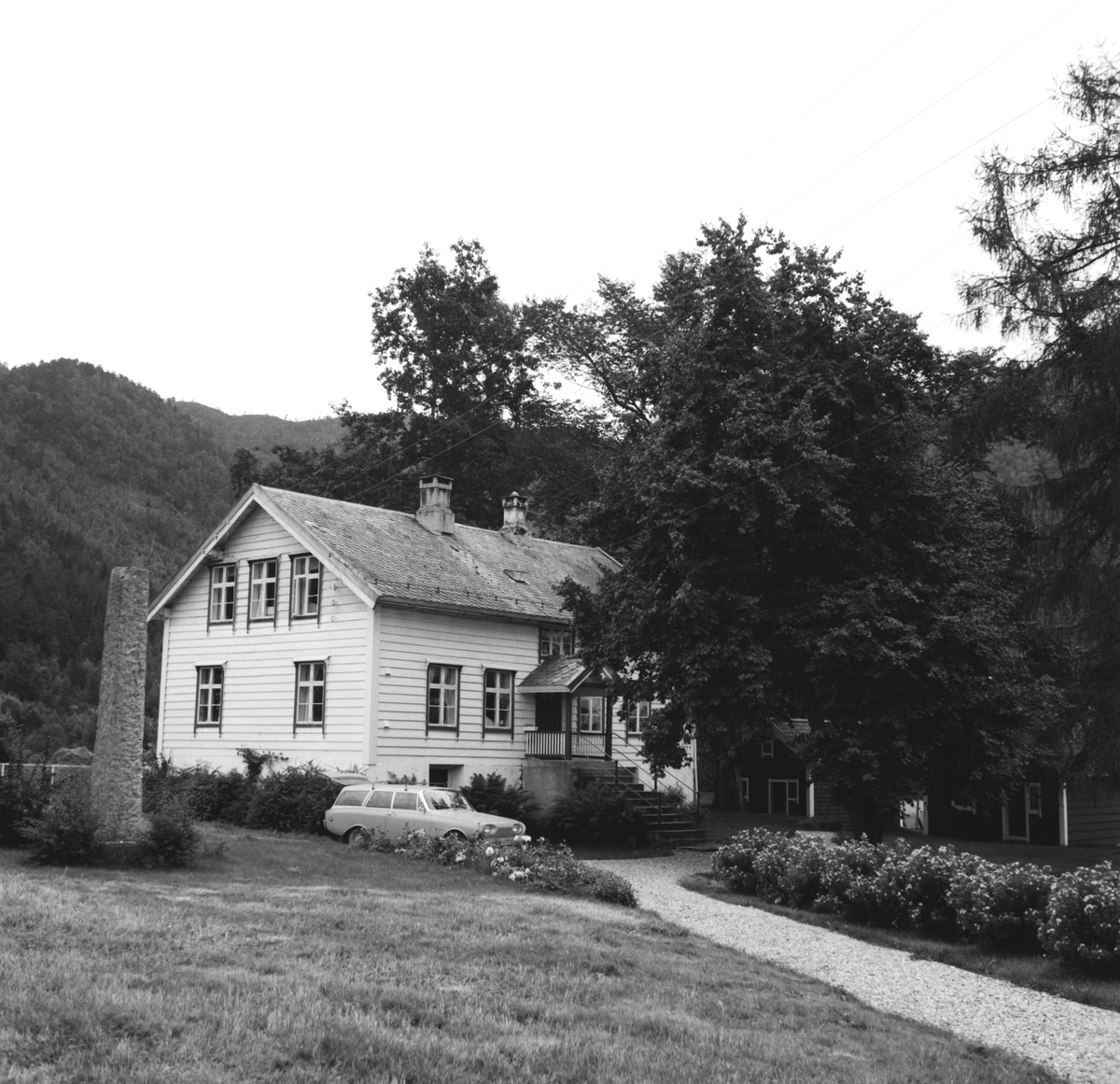 Prospektfotografi av et våningshus med stabbur og uthus på gården Vassbotn. Ved huset står en bautastein.
