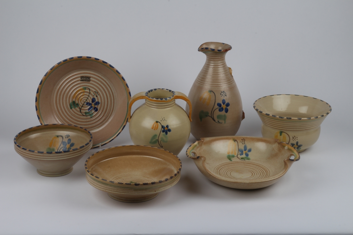 Dekketøy fra Ganns keramikk bestående av kaffekopp med underskål, asjett, smørbrødbrikke, sukkerskål, mugge, skål, fruktfat, vase og potteskjuler.