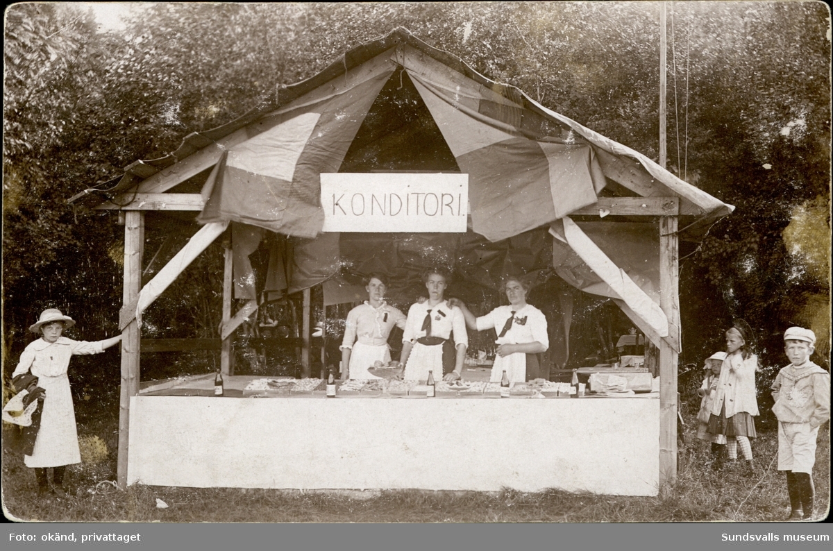 Vykort med motiv av ett marknadsstånd med skylten konditori. Enligt texten på baksidan: Wärstaparken 26 juli 1914.