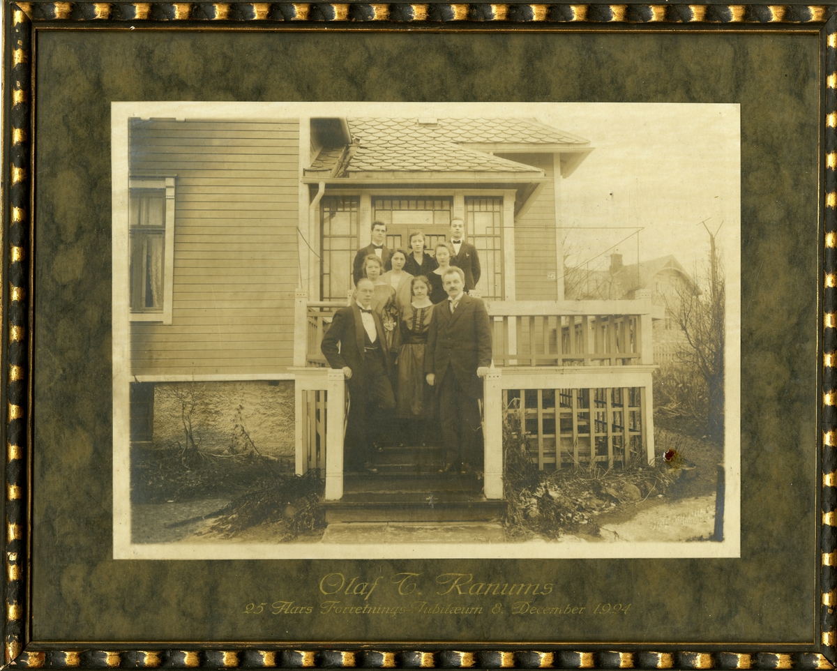 Bildet viser familien Ranum, med ansatte, i anledning Olaf T. Ranum a/s sitt 25 års jubileum i 1924. Ranum Sr fremst til høyre på bildet. Gruppen står utendørs på en trapp foran en veranda. Det er litt snø på bakken.